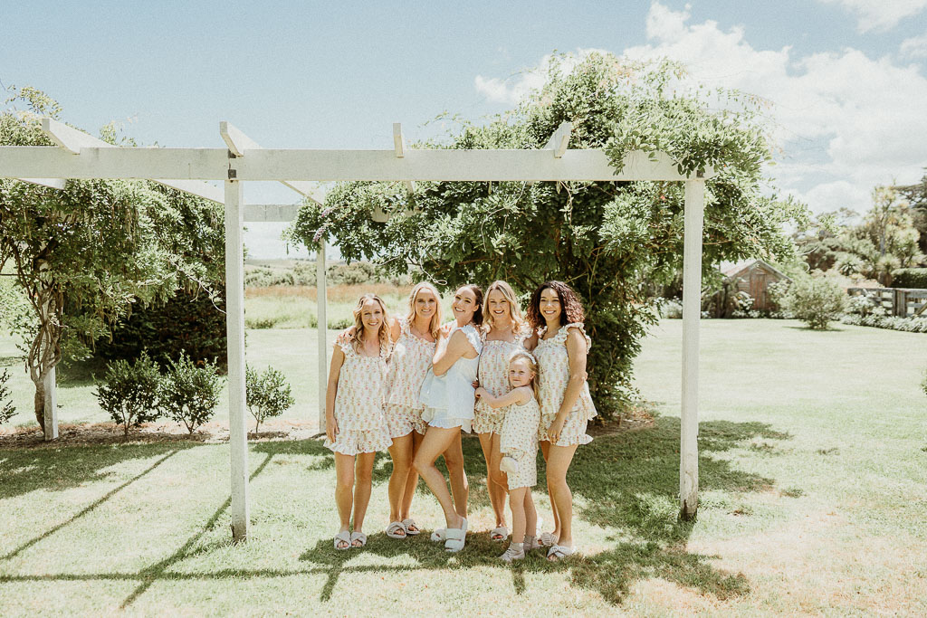 Bride and bridesmaids enjoying a joyful moment under a pergola in a lush garden, perfectly organized by an On the Day Wedding Coordinator Adelaide.