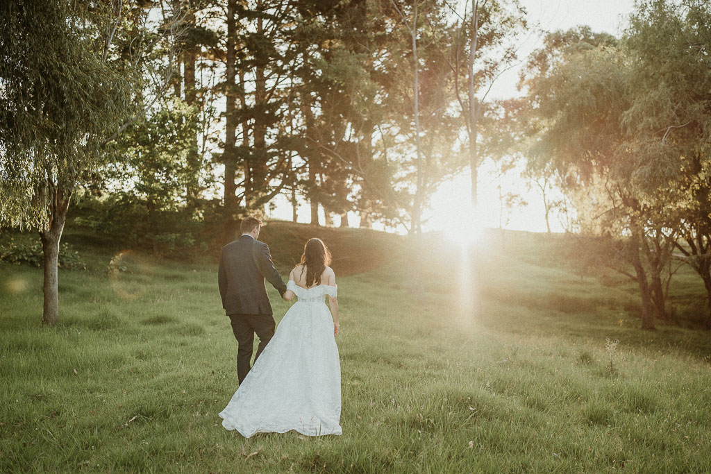 Bride and groom walking hand in hand through a sunlit meadow, capturing a romantic moment planned by an On the Day Wedding Coordinator Adelaide.