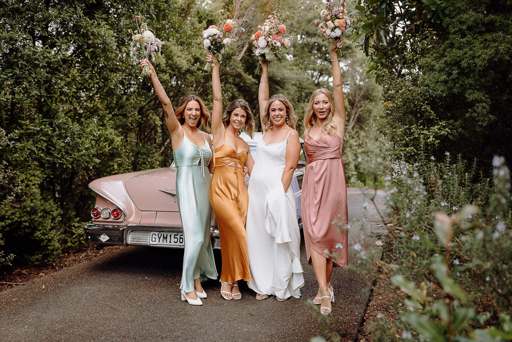 Bride and bridesmaids posing with vibrant bouquets in front of a classic vintage car, showcasing the seamless coordination of an On the Day Wedding Coordinator Brisbane.