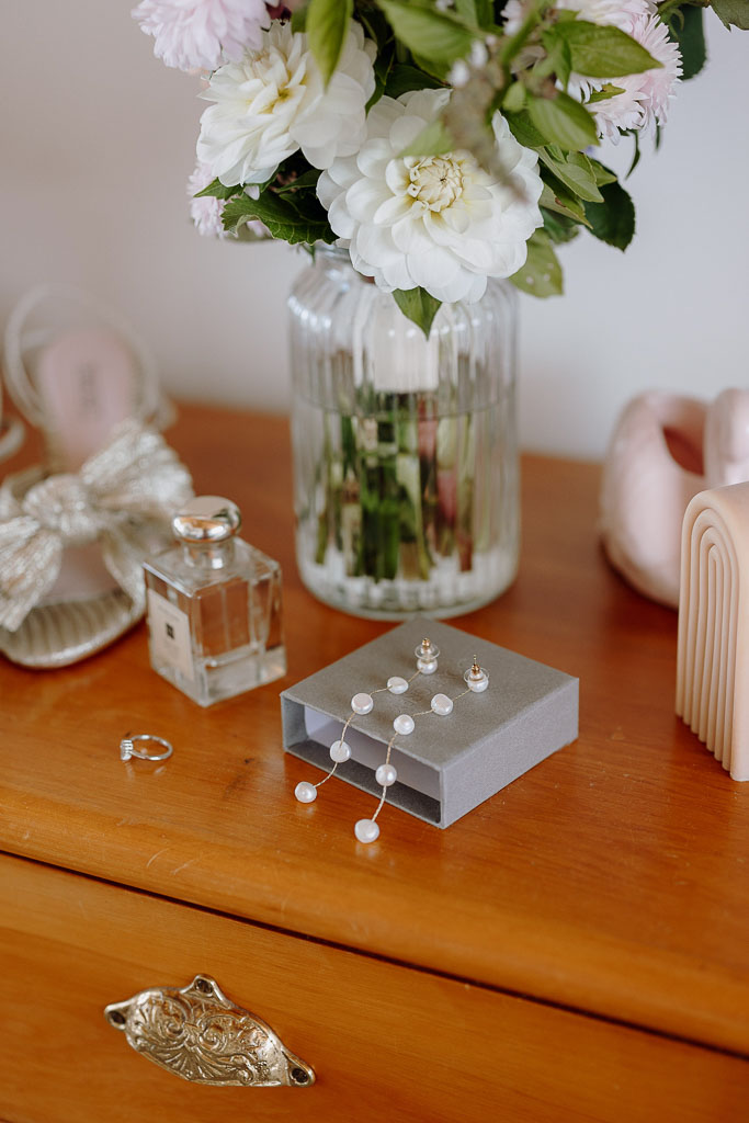 Elegant bridal accessories including pearl earrings, perfume, and floral arrangements, thoughtfully curated by an On the Day Wedding Coordinator Brisbane.