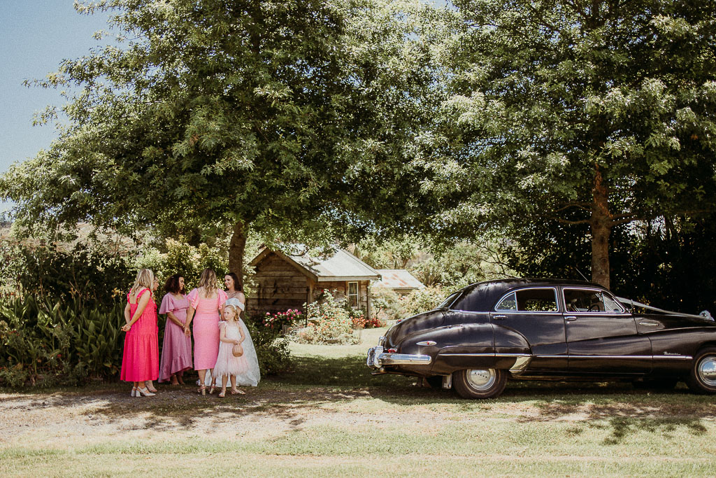 Bridesmaids and flower girl gathered near a classic vintage car under a shady tree, enjoying a beautifully coordinated moment by an On the Day Wedding Coordinator Perth.